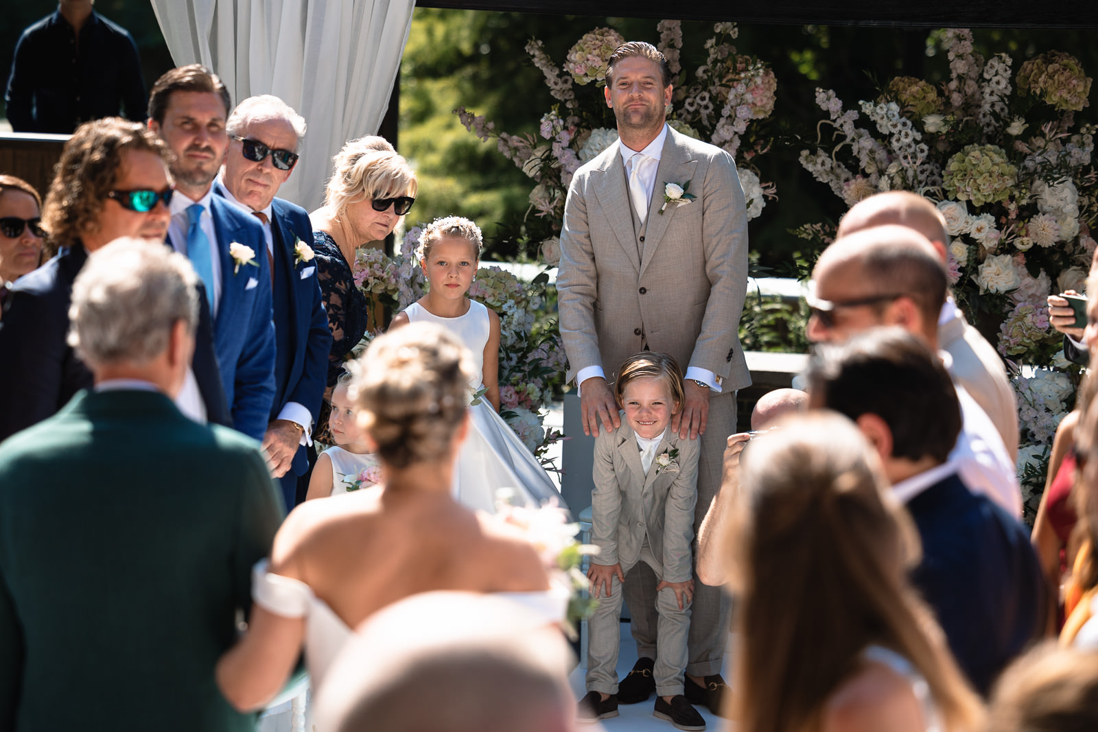 Bruidegom met zoon stralen terwijl bruid met vader oploopt voor Opkomst bruidegom met zoontje voor romantische ceremonie trouwfotograaf den haag