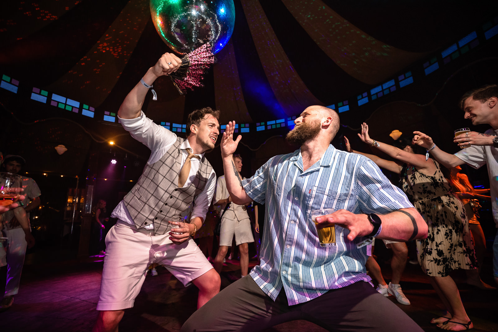 Huwelijksfeest bruidegom en vriend met waaier in spiegeltent festival bruiloft trouwfotograaf Camping de Lievelinge