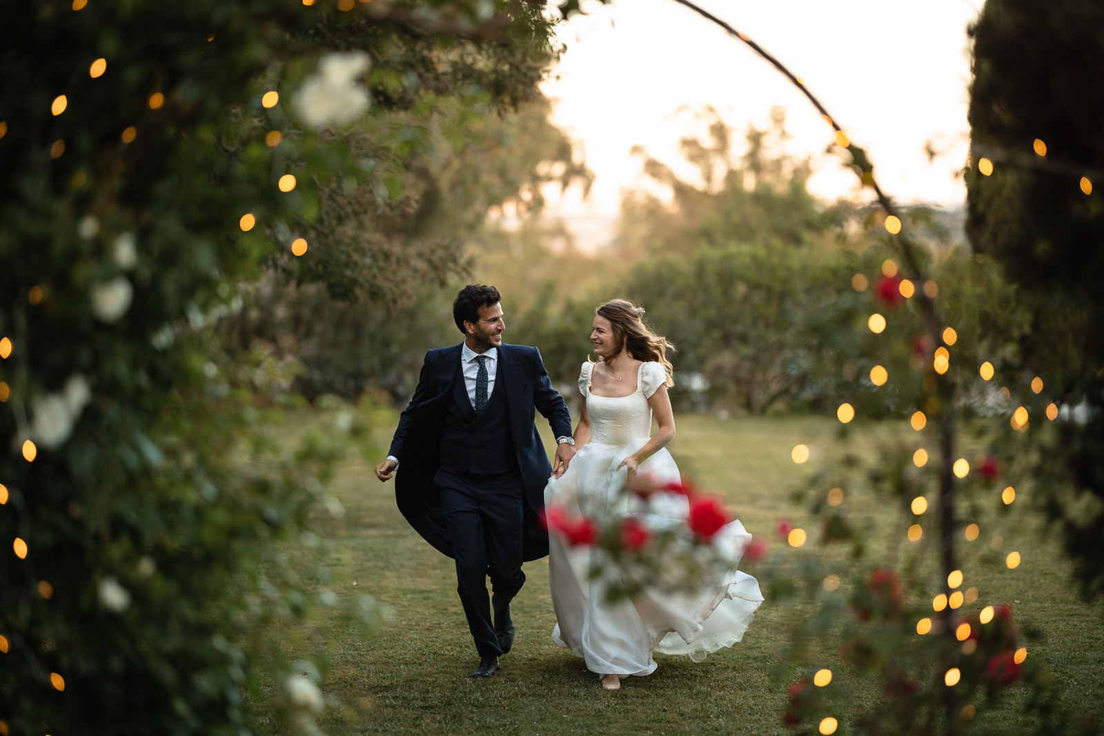 Golden hour fotomoment met bruidspaar en bloemenboog met lampjes bij Destination Wedding Las Jarillas Madrid